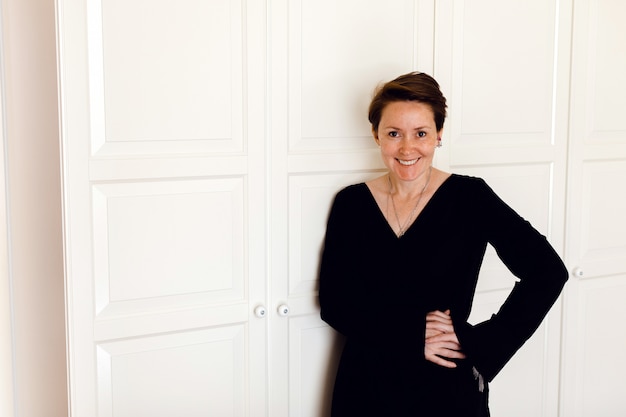 Cheerful woman with hands on waist against white closet doors