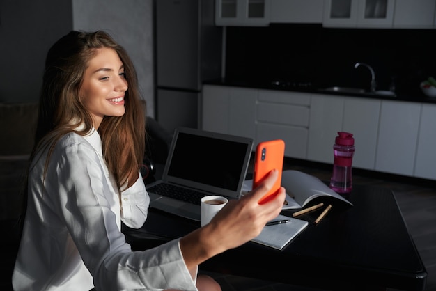 Cheerful woman with long hair doing selfie on modern smartphone while staying at home