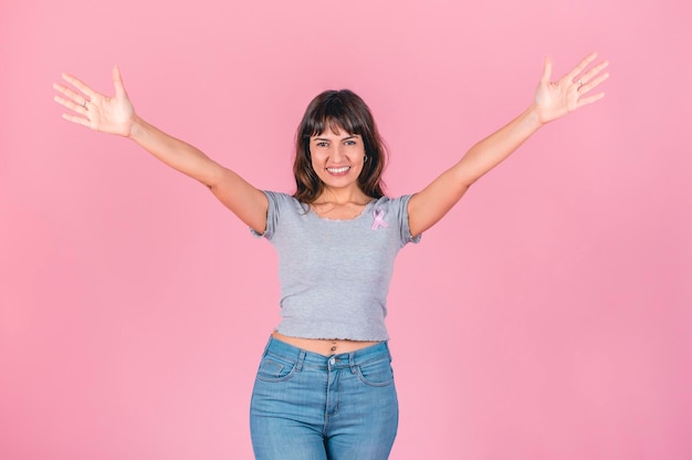 Photo cheerful woman with open arms wearing a breast cancer pink ribbon over pink background victory to breast cancer concept