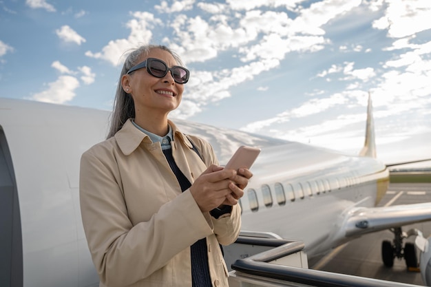 Donna allegra con il telefono in piedi all'aperto in aeroporto e distogliendo lo sguardo