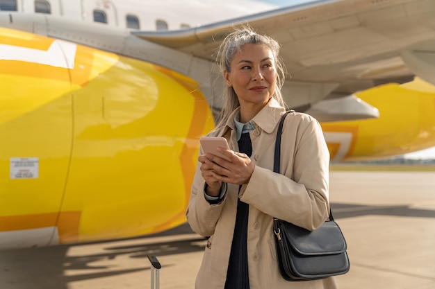 写真 空港で屋外に立って、目をそらしている電話を持つ陽気な女性