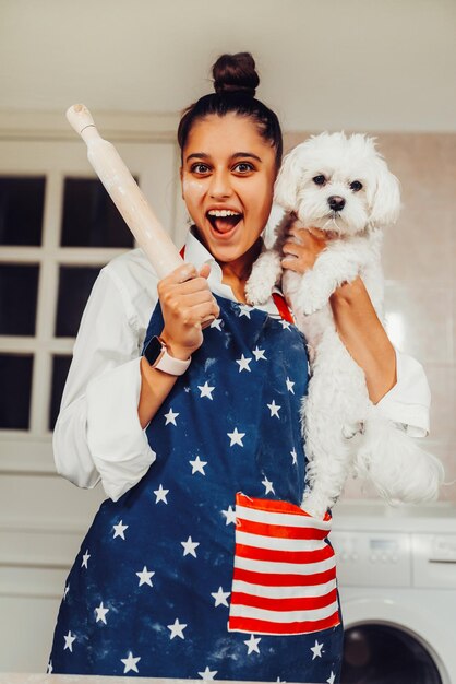 Foto donna allegra con un mattarello e un cane maltese bianco