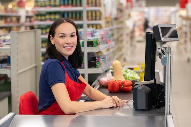 Cheerful woman working in supermarket sitting at cash desk