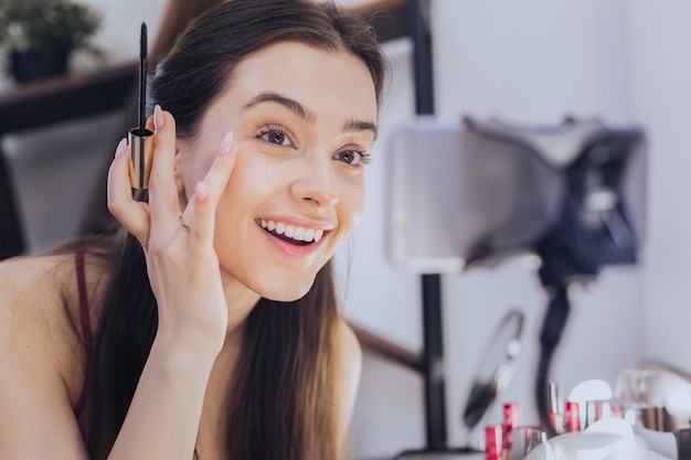 Cheerful woman. Young cheerful woman smiling broadly while filming blog about new cosmetics