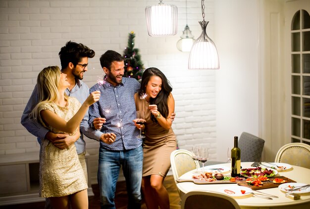 Cheerful women and men celebrating New Year eve with sparkles and wine