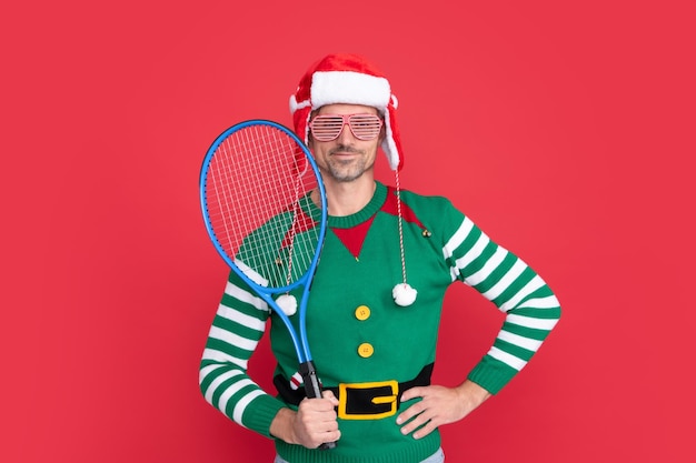 Foto allegro ragazzo di natale tenere il razzo da tennis su sfondo rosso felice anno nuovo buon natale