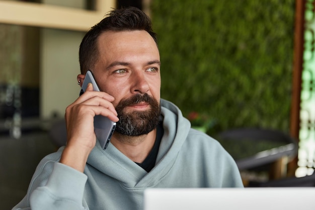 Cheerful young adult man in casual clothes in cafe talking on a mobile phone