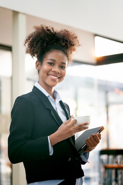 Cheerful young African American Businesswoman holding coffee cup and tablet pc smiling at camera Wireless technology concept