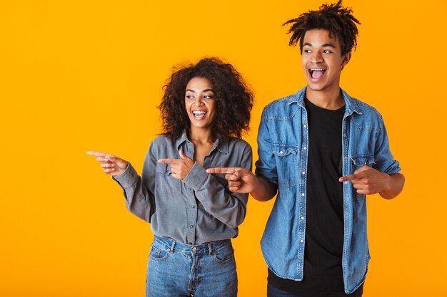 Cheerful young african couple standing isolated, pointing fingers at side