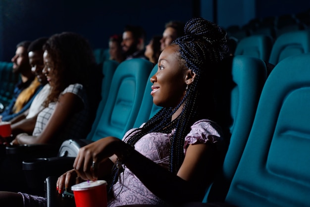 Cheerful young African woman smiling while enjoying a movie at the local cinema