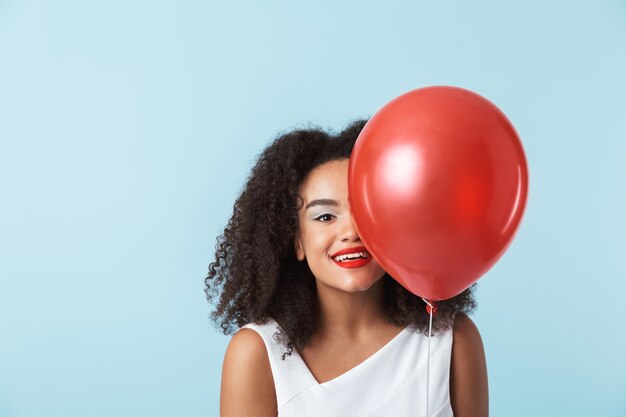 Cheerful young african woman wearing dress celebrating, holding balloon isolated