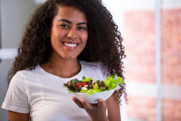 cheerful young afro american woman eating vegetable salad in home kitchen.