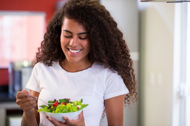 Allegra giovane donna afro americana che mangia insalata di verdure nella cucina di casa