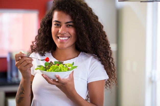 家庭の台所で野菜サラダを食べる陽気な若いアフリカ系アメリカ人女性