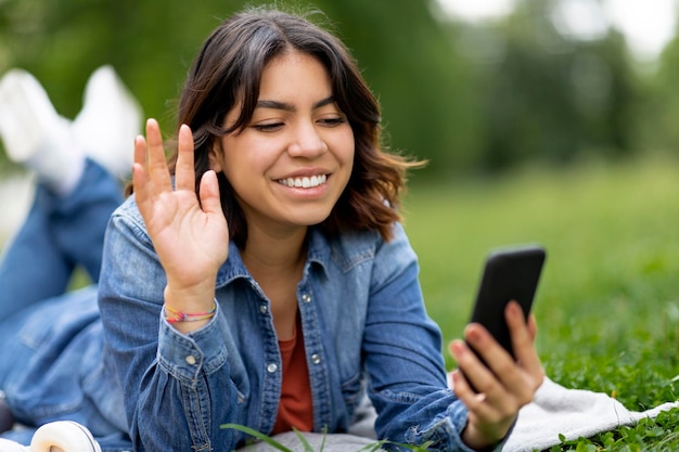 屋外のクローズ アップ ショットのスマート フォンでビデオ通話を行う陽気な若いアラブ女性