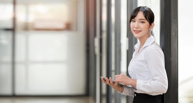 Cheerful young asian businesswoman holding digital tablet and looking at camera