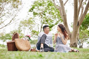 Cheerful young asian couple in love resting on blanket in park and talking