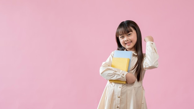 陽気な若いアジア人の女の子が本を持ち、握りこぶしを見せている