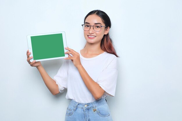 Cheerful young Asian girl in white tshirt showing digital tablet with empty screen isolated on white background