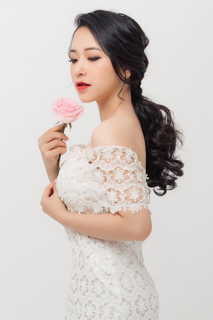 Cheerful young Asian lady wearing white dress and holding flower bouquet over white background