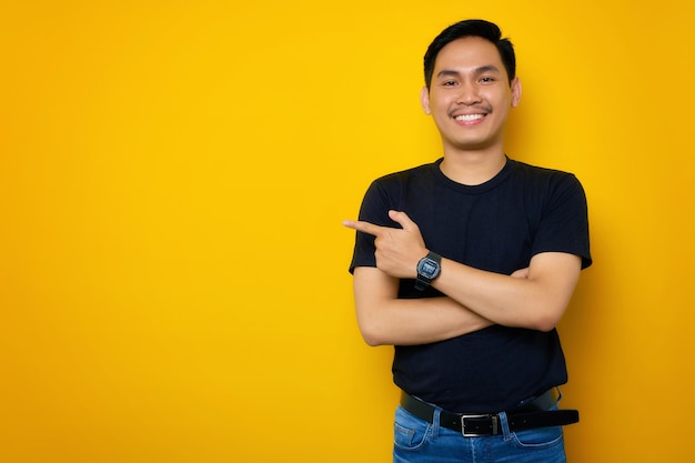 노란색 배경에 격리된 복사 공간에서 손가락을 옆으로 가리키는 캐주얼 티셔츠를 입은 쾌활한 젊은 아시아 남자 Great offer concept