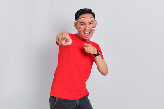 Cheerful young Asian man celebrating Indonesian independence day pointing at camera isolated on white background