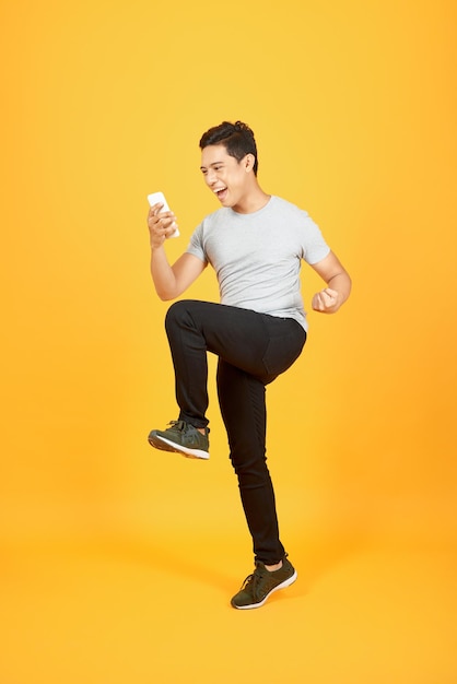 Cheerful young Asian man dressed in tshirt jumping over orange background make winner gesture