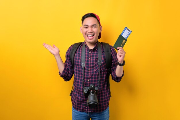 Cheerful young Asian man with backpack holding passport and flight tickets isolated over yellow background Tourism and holiday trip concept