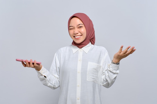 Cheerful young Asian Muslim woman using mobile phone and celebrating success getting good news isolated over white background