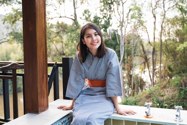 Cheerful young asian woman in bathrobe sitting on natural hot spring pool among the nature at the resort