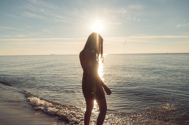 Cheerful young asian woman in brown dress with sunshine glowing on the beach in tropical sea on summer vacation