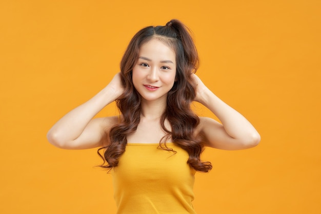 Cheerful young asian woman girl in yellow crop top posing isolated on yellow background.