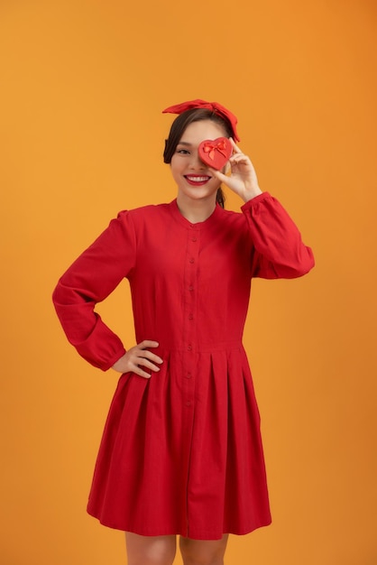 Cheerful young Asian woman holding gift box when standing over orange background