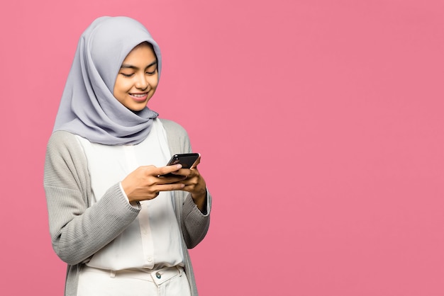 Cheerful young Asian woman holding mobile phone and smiling looking on screen