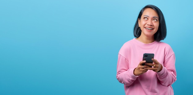 Photo cheerful young asian woman holding smartphone and happy looking aside