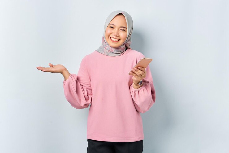 Cheerful young Asian woman in pink shirt using mobile phone reading news from social network isolated over white background