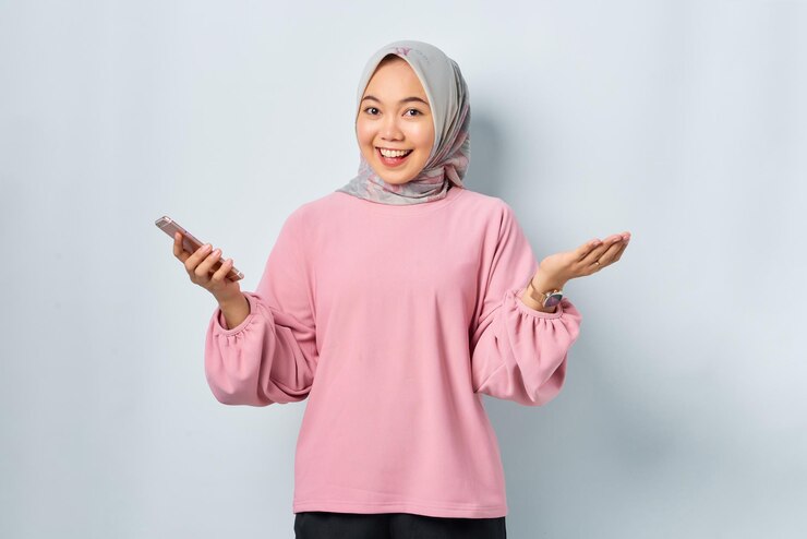 Cheerful young Asian woman in pink shirt using mobile phone reading news from social network isolated over white background