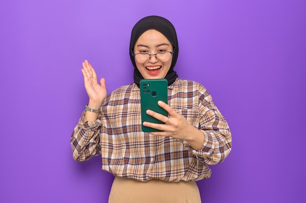 Cheerful young Asian woman in plaid shirt using a mobile phone getting good news isolated on purple background