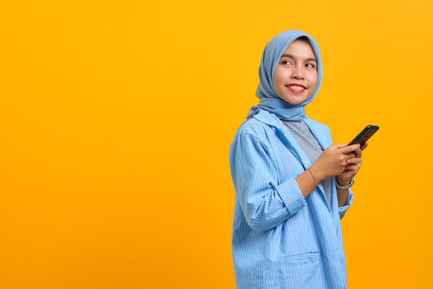 Cheerful young Asian woman using mobile phone and looking aside at empty space