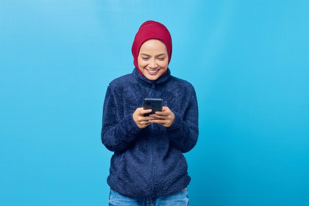 Cheerful young Asian woman using smartphone on blue background