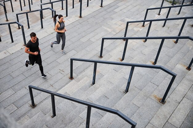 Cheerful young athletic man and woman running together upstairs during training outdoors