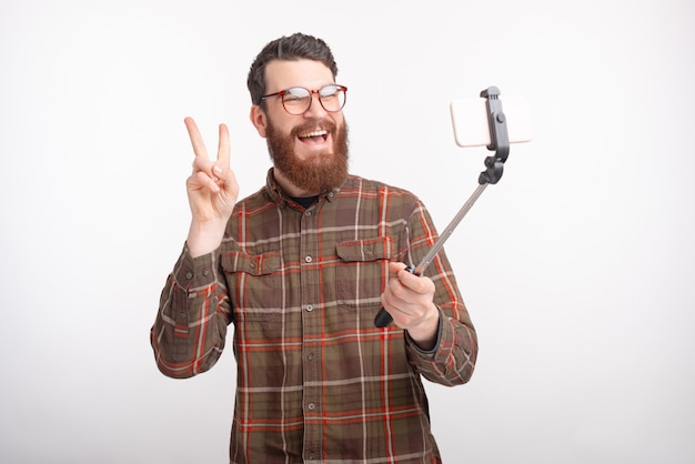 Cheerful young bearded man is making a photo with selfie stick n white space.