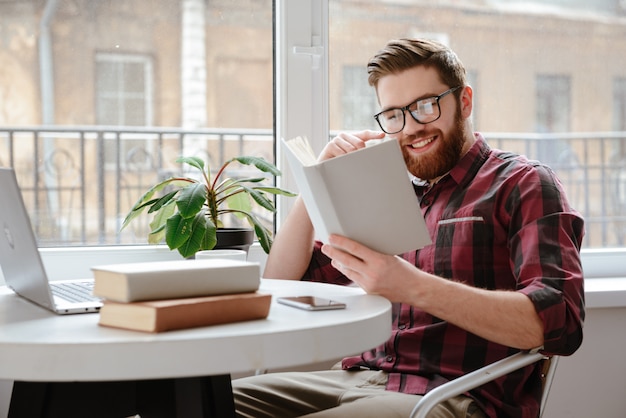 Cheerful young bearded man reading books.