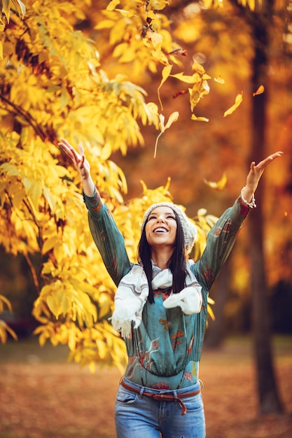 Cheerful young beautiful woman going alone in the park and throws leaves up in golden sunny autumn.