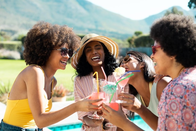 Cheerful young biracial female friends toasting cocktails while having fun at summer pool party