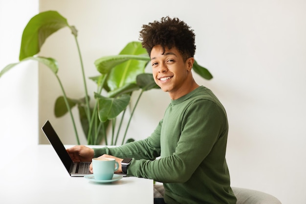 Cheerful young black guy freelancer working from cozy cafe