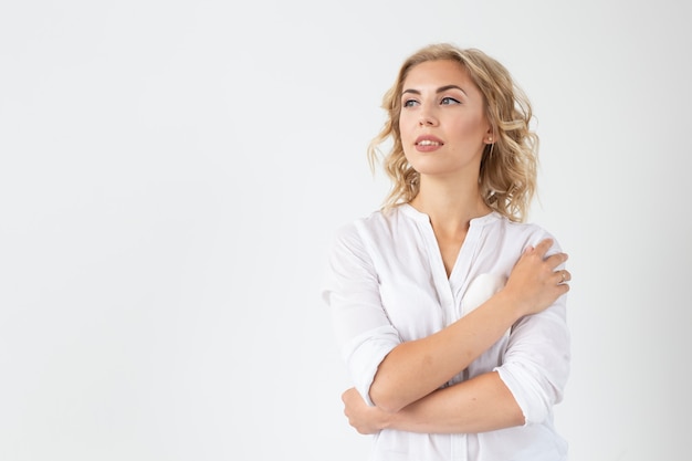 Cheerful young blond woman with long curly hair posing on a white surface with copy space the