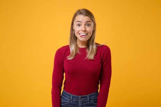 Cheerful young blonde woman girl in casual clothes posing isolated on yellow orange wall background studio portrait. People sincere emotions lifestyle concept. Mock up copy space. Showing tongue.