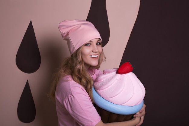 Cheerful young blonde woman having fun with big cupcake sweet decoration