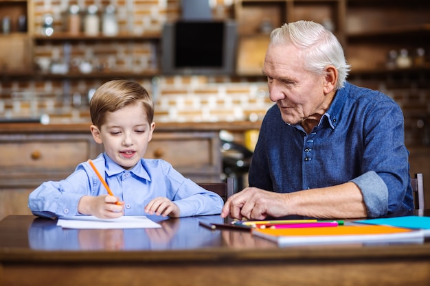 Cheerful young boy drawing with his grandfather while spending weekend together